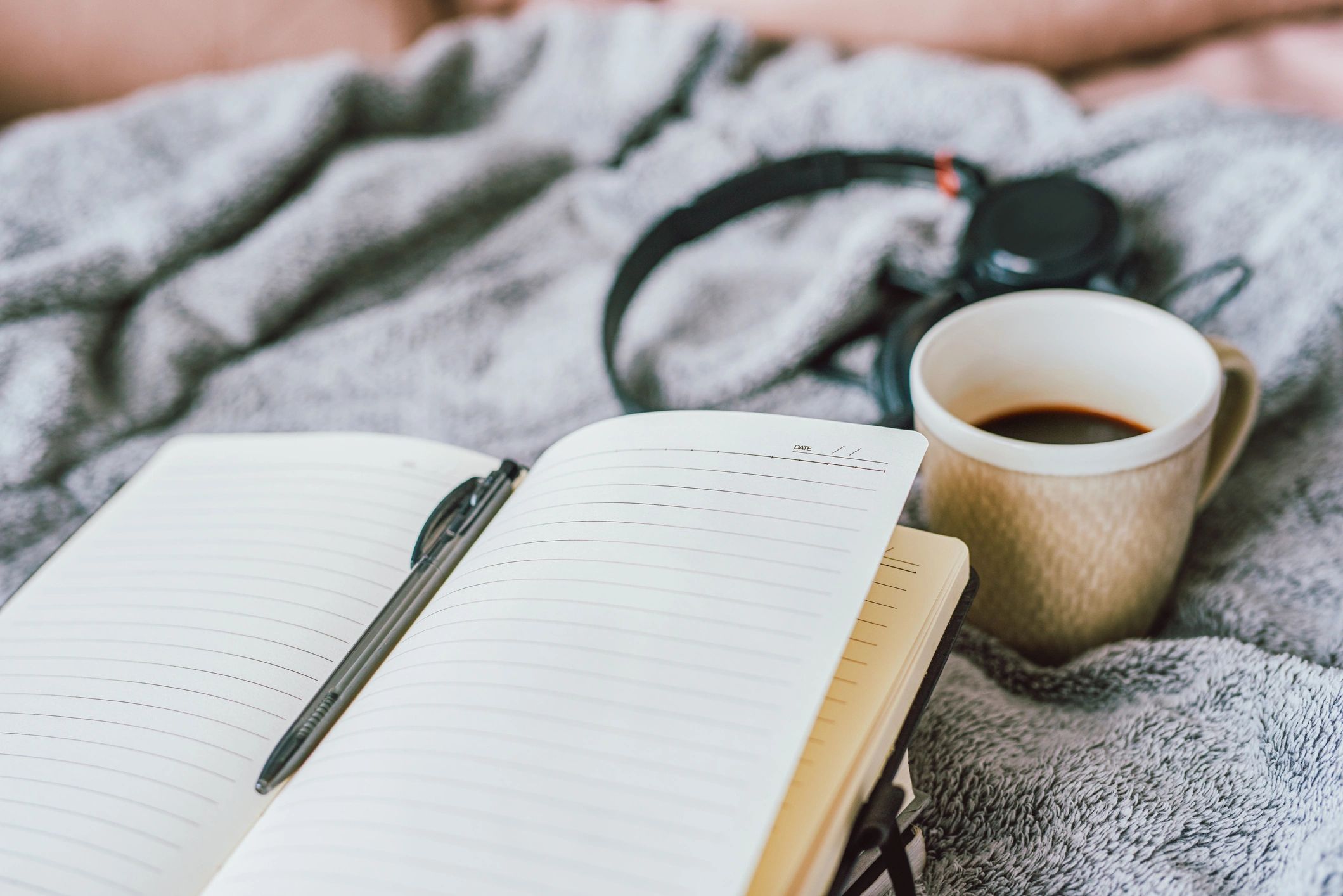 Hands writing in a notebook beside a cup of coffee