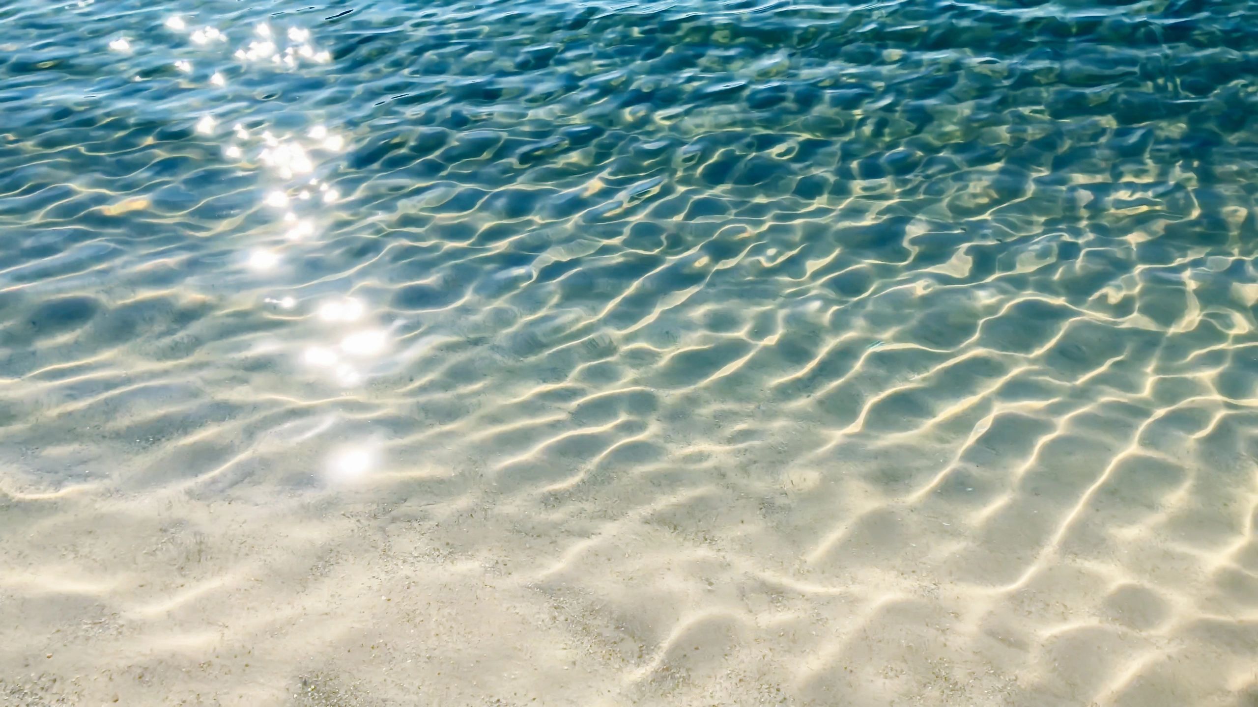 Sunlight glittering on rippled blue water near a white sand beach