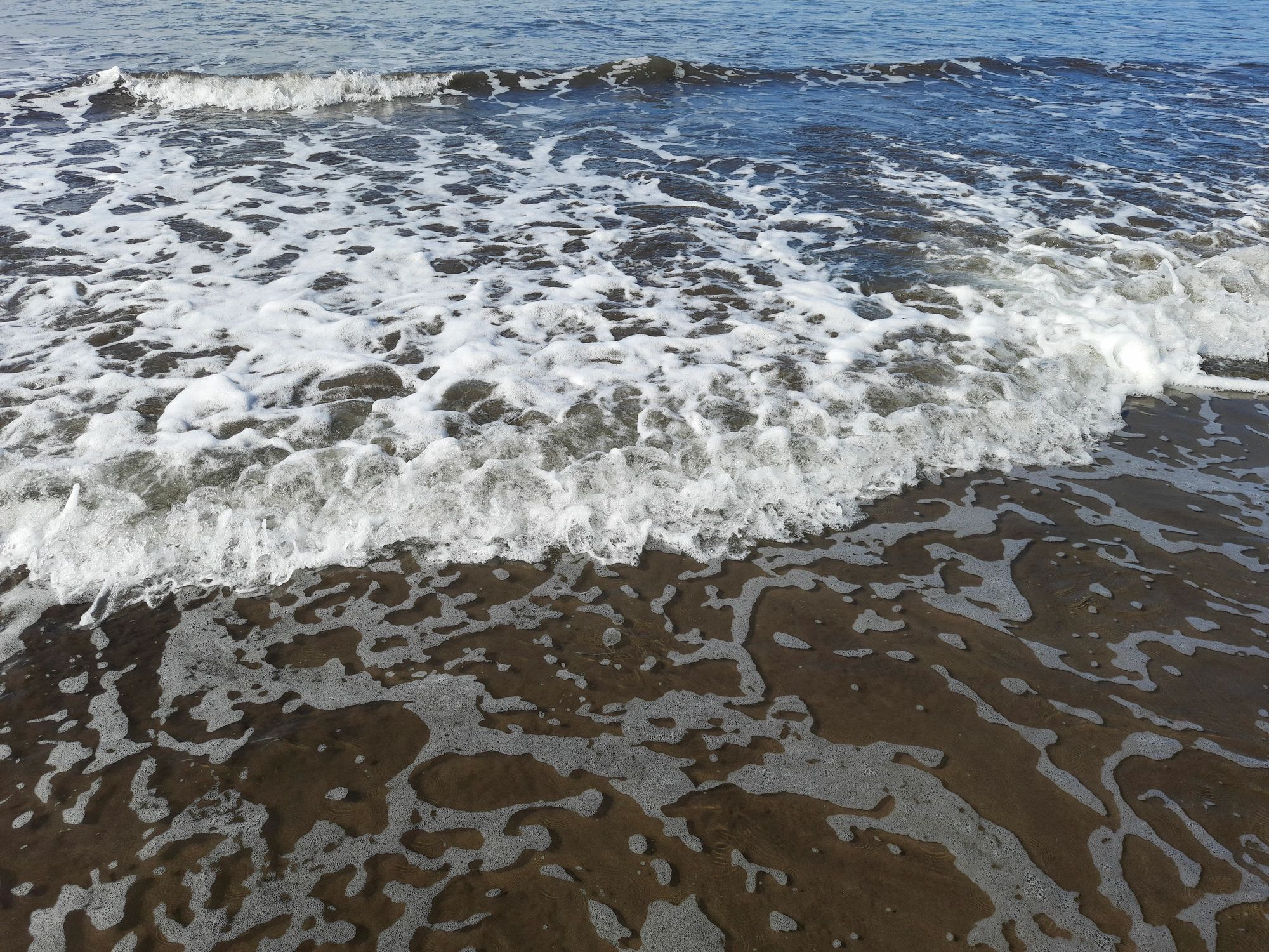 Ocean waves breaking on a sandy beach with white foam patterns